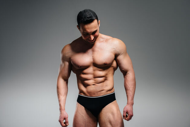 身体一个年轻的健美运动员赤裸上身在摄影棚里摆姿势 炫耀他的腹肌和肌肉运动躯干运动二头肌