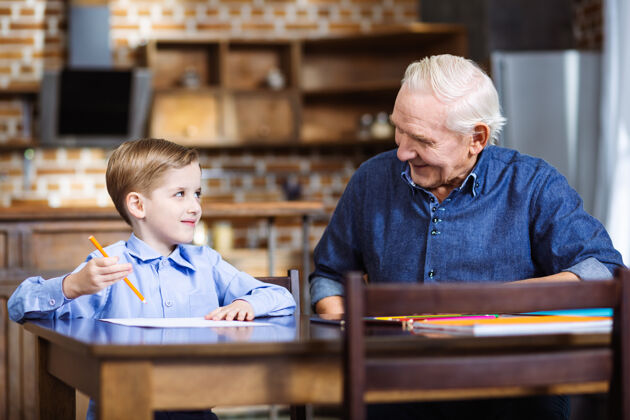 心情快乐的小男孩在画画 而他的祖父坐在附近纸张一起欢呼