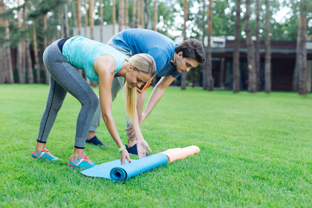 生态准备锻炼积极的年轻人在准备锻炼的同时把瑜伽垫放在草地上积极浪漫快乐