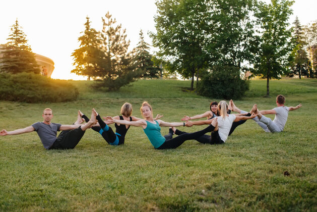 活动日落时分 一群人在公园里进行成对的瑜伽练习健康的生活方式 冥想和健康草地年轻健身