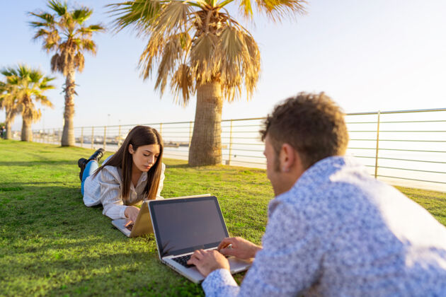 空间一对年轻的夫妇躺在草地上 在日落或黎明时面面相觑地使用笔记本电脑智能个人电脑使用