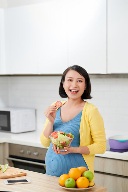中国快乐的孕妇在厨房做健康沙拉女性腹部有机