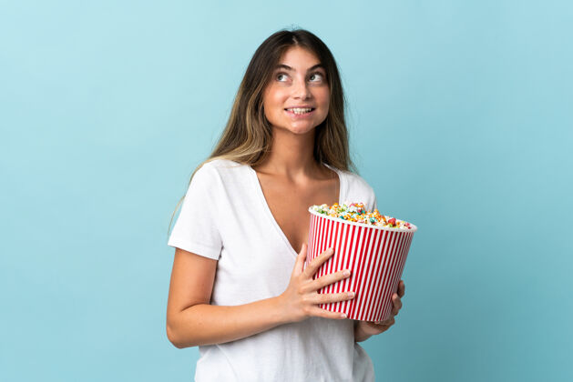 电影一个年轻的高加索女人被隔离在蓝色的墙上 手里拿着一大桶爆米花爆米花漂亮女性