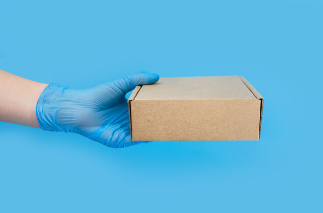 盒子手在一个蓝色的手套举行一个纸板箱在一个蓝色的表面复制空间包装安全卫生