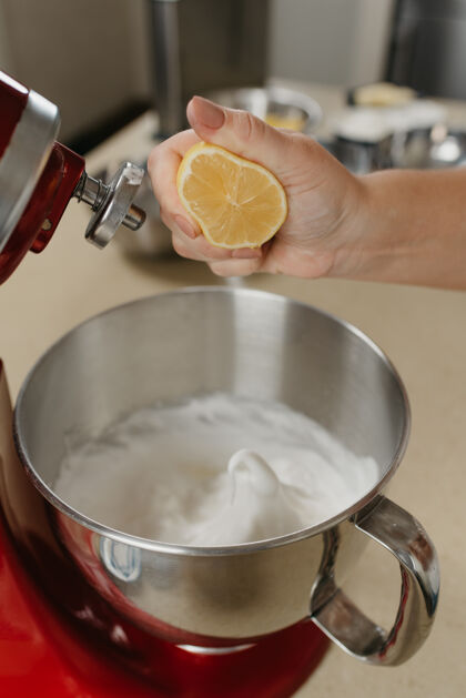 配料一个年轻女子的手粉碎柠檬汁的不锈钢碗在厨房混合蛋白酥皮的亲密照片柠檬厨师白