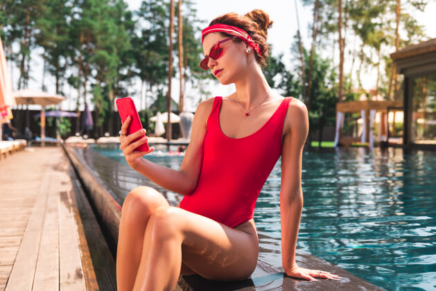 周末电子设备坐在游泳池边 用着她现代化的智能手机的漂亮可爱的年轻女人创新漂亮休息