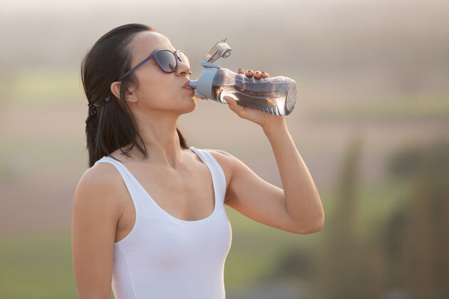 自然在徒步旅行时 一个女人正在休息 喝着水瓶里的水 站在岩石山脊上 眺望着山谷活动饮用人