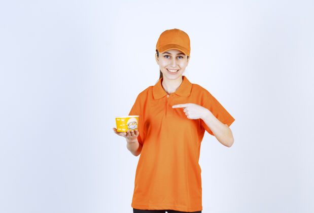 员工穿着黄色制服的女快递员拿着一个外卖面杯子指着它订单姿势食品