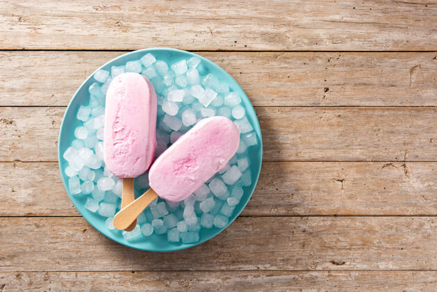 果汁草莓冰棒和碎冰放在蓝色盘子和木桌上压碎夏天草莓