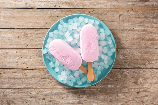 零食草莓冰棒和碎冰放在蓝色盘子和木桌上奶油棍子夏天