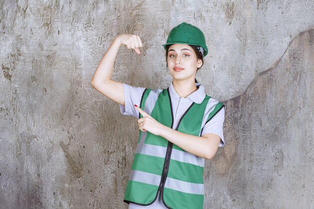 员工穿着绿色制服和头盔的女工程师展示她的手臂肌肉工人成功人体模特