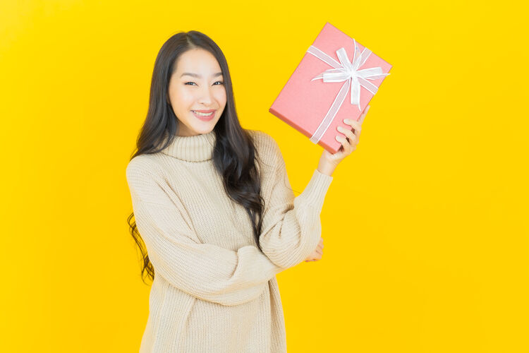 时尚肖像美丽的亚洲年轻女子微笑着黄色墙上的红色礼盒时尚礼物新的