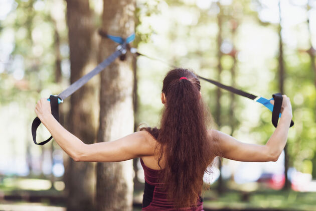 教练一位年轻女子在公园里的一棵树上的高架机器上锻炼背部肌肉磁带运动员女人