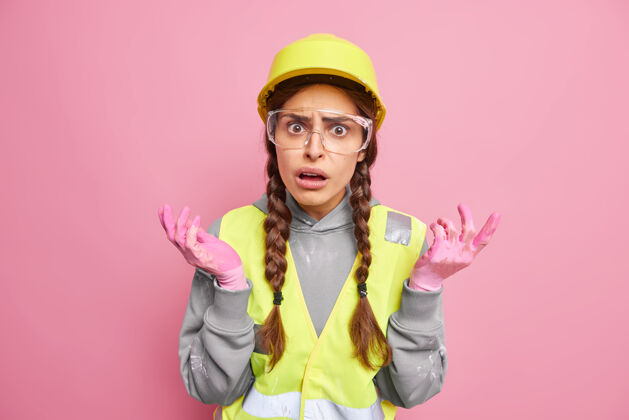 技术员愤愤不平的女建筑工人工业工人耸耸肩感到困惑摊开双手侧戴安全帽眼镜反光背心在工厂或工地工作工程师表情成功
