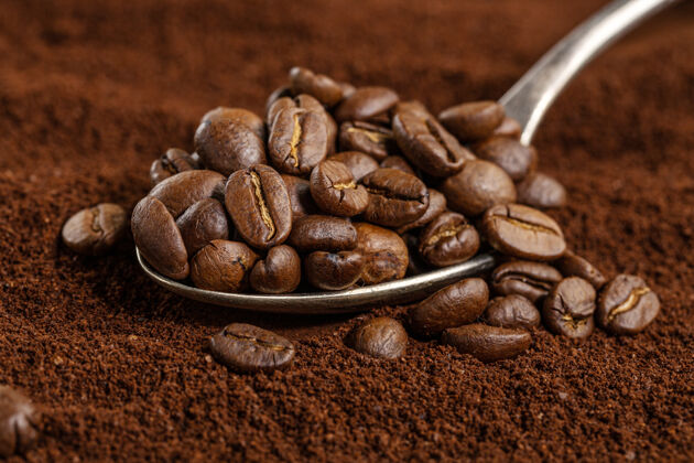 堆咖啡豆放在勺子上放在咖啡粉上特写芳香摩卡咖啡馆