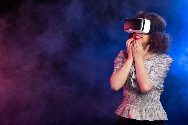 穿着年轻女性戴着虚拟现实耳机在黑烟上玩电子游戏年轻女性美丽姿势