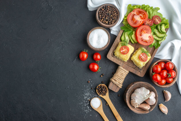 容器俯视图切割整个新鲜西红柿和黄瓜奶酪在木板餐具集调味品在勺子在黑色表面香料餐厅晚餐