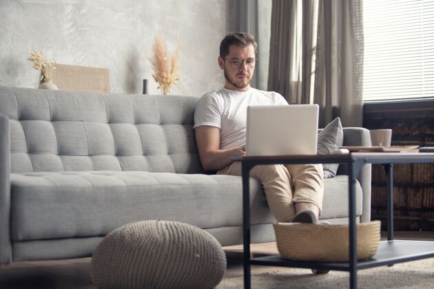 舒适帅哥坐在家里的沙发上微笑着用笔记本电脑放松电脑家庭