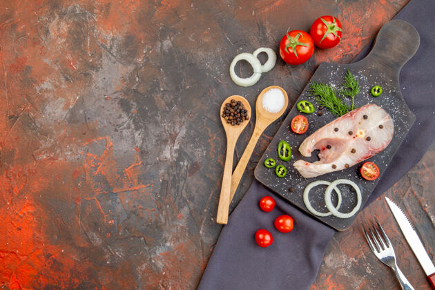 午餐前视图生鱼和胡椒洋葱绿色西红柿在黑色切割板上毛巾餐具设置在混合颜色的表面混合餐具木勺
