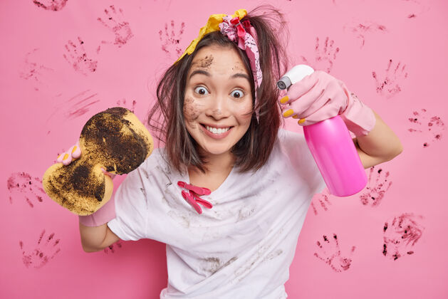 家务快乐的少女 带着马尾微笑 快乐地用洗衣粉和海绵清洗隐形表面 穿着白色斑点t恤 脏脸站在粉红色的地面上服务女士设备