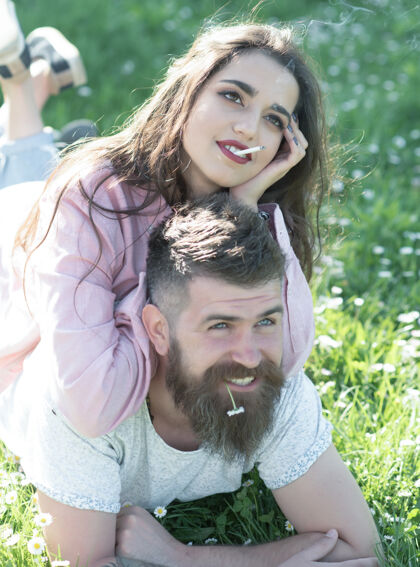 胡须一对幸福的情侣躺在绿草草地上 男人和女友一起享受阳光明媚的日子 户外春意盎然黑发时髦雏菊