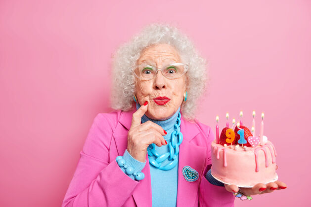 场合美丽的老卷发女人穿着化妆红色唇膏 身着时髦的服装 透明的玻璃杯上放着燃烧着的蜡烛 庆祝她的生日高级生日积极