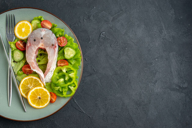 午餐半张生鱼片和新鲜蔬菜柠檬片和餐具放在黑色表面左侧的灰色盘子上 有自由空间晚餐餐具壁板