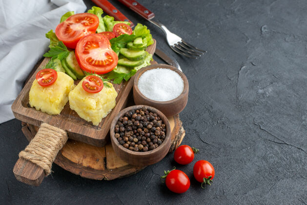 西红柿切碎的和整个新鲜蔬菜的特写镜头切菜板上的奶酪和香料餐具设置在黑色表面膳食晚餐新鲜蔬菜