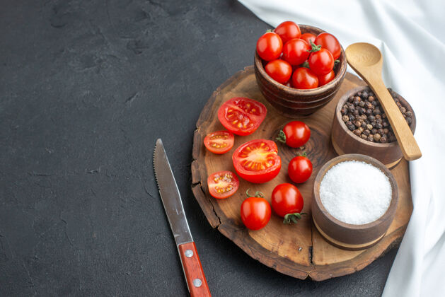 左全切新鲜西红柿和香料在木板上的正面图白色毛巾刀在左侧黑色表面上有自由空间健康西红柿整个