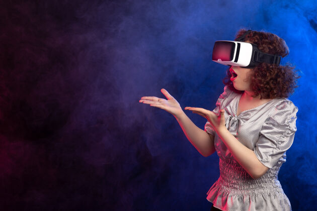 美丽年轻女性戴着虚拟现实耳机在黑烟中玩游戏视频穿着舞蹈表演