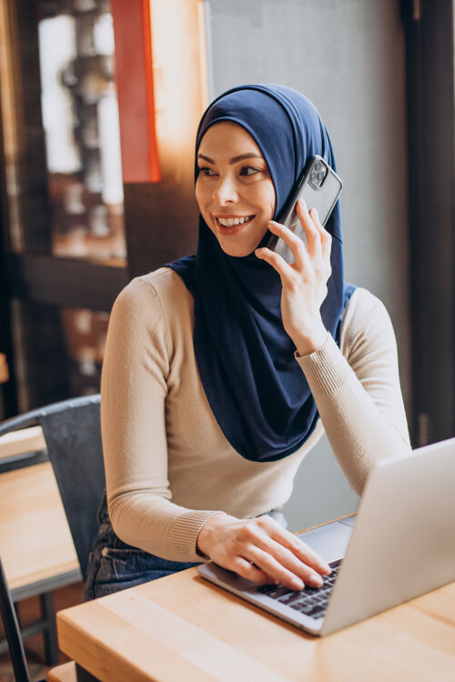手机年轻的妇女在咖啡馆里用电话和电脑漂亮传统