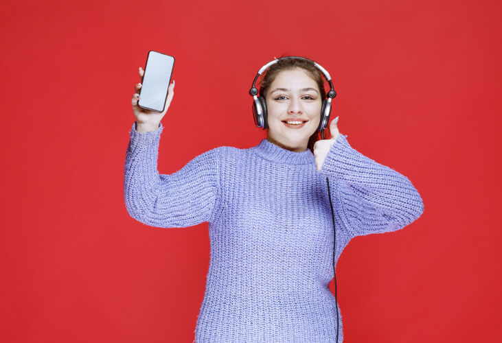 技术戴着耳机的女孩展示着她的智能手机 感觉很开心女性智能女性