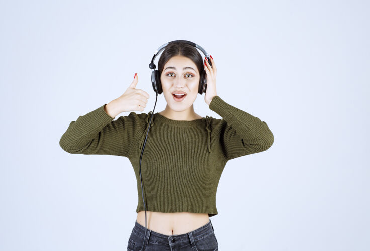 女孩戴着耳机听音乐竖起大拇指的年轻女孩的画像表达年轻音乐