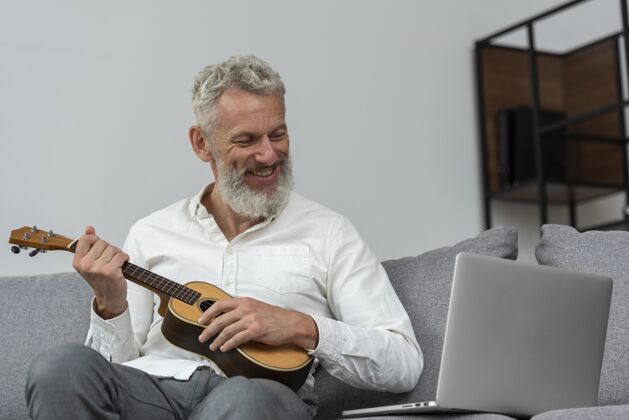 成人在家学习四弦琴课程的资深男子在笔记本电脑上水平学习灰色头发