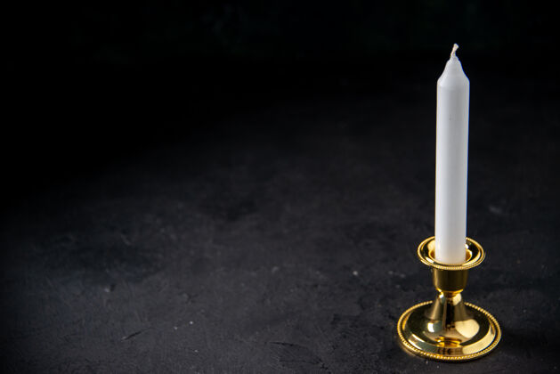 黑暗前视图中的白色蜡烛在黄金插入黑色火焰烛台火