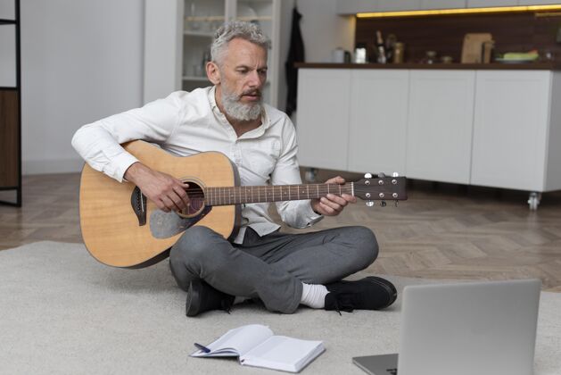 研究大四的男人在家地板上学吉他成人室内家庭