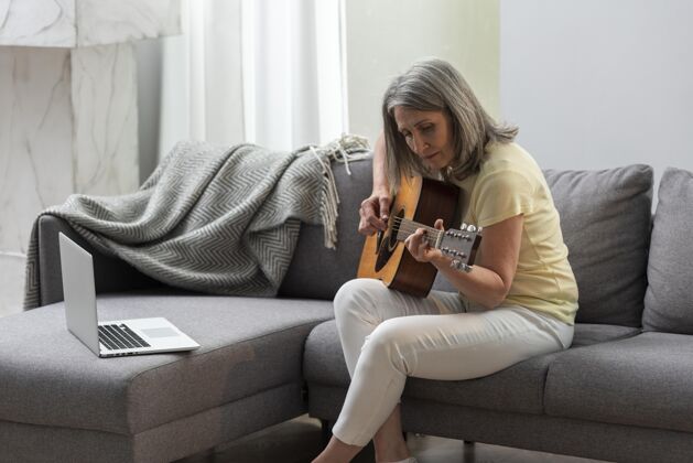 养老金资深女士在家沙发上用笔记本电脑上吉他课老年人吉他课成熟
