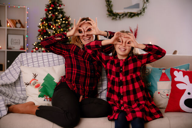 坐着笑眯眯的母女俩坐在沙发上看着手指 在家里享受圣诞节时光女儿微笑享受