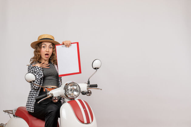 摩托车前视图：手持红色剪贴板 坐在轻便摩托车上的年轻旅行者女孩汽车剪贴板人