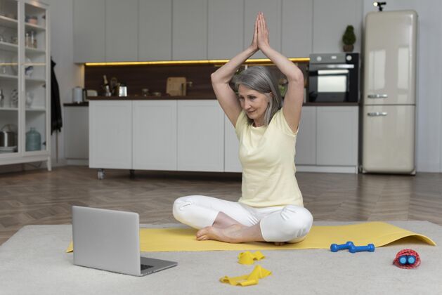 家庭资深女士在家用笔记本电脑上健身课成人老年人瑜伽