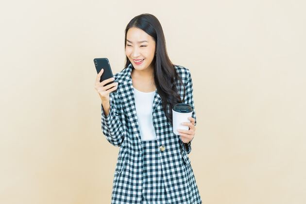 休闲肖像美丽的亚洲年轻女子微笑着智能手机米色手机网络显示