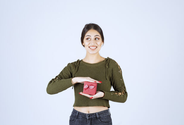 年轻微笑的女人拿着礼品盒 看着白色背景上的相机礼物惊喜盒子