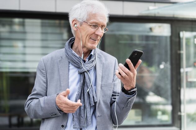 设备时尚的老男人在城市使用智能手机和耳机的视频通话成熟老年人移动