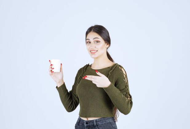 杯子一个年轻漂亮的女模特指着一个装着热饮的塑料杯年轻漂亮女人