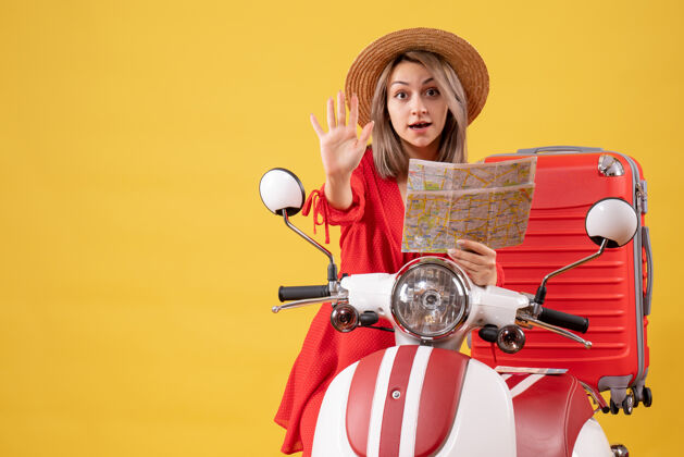 持有正面图：身穿红色连衣裙的年轻女士手持地图 站在轻便摩托车旁做停车标志旅行者站立旅游者