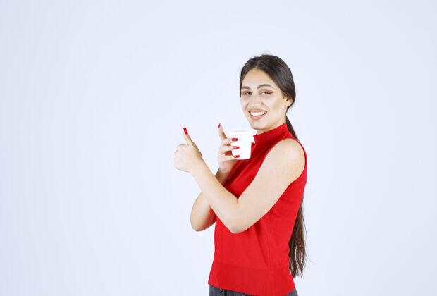 休闲穿红衬衫的女孩在喝咖啡 并表现出积极的迹象享受模特工人
