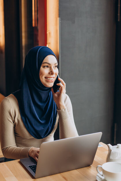 伊斯兰年轻的妇女在咖啡馆里用电话和电脑科技手机女性