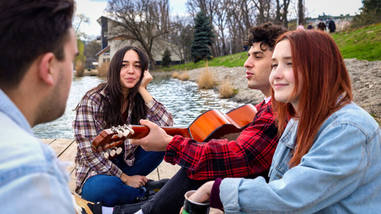 运动四个年轻的朋友在公园的湖边唱歌 休息 弹吉他公园夏天未知