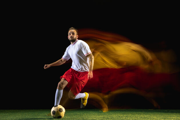 运动员建议年轻的白人男子足球或足球运动员穿着运动服和靴子踢球的目标在混合光暗墙上健康的生活方式 职业体育 爱好的概念活动比赛球衣