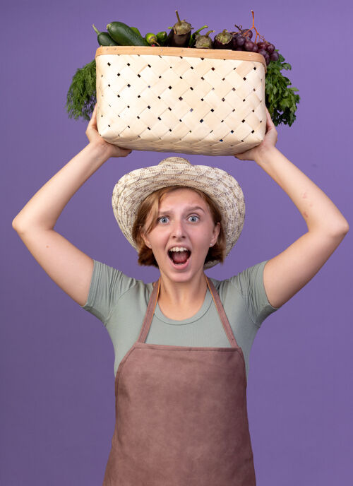 蔬菜焦急的年轻斯拉夫女园丁戴着园艺帽 头顶着菜篮子女性穿紫色